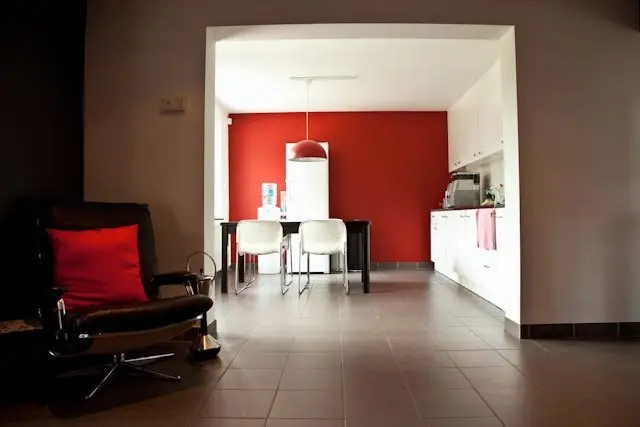 Een zithoek met een fauteuil en zicht op de keuken met eettafel en rode wand